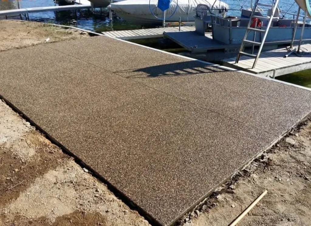 Newly installed, textured dock surface extending to the water, surrounded by dirt and wooden dock structures in the background.