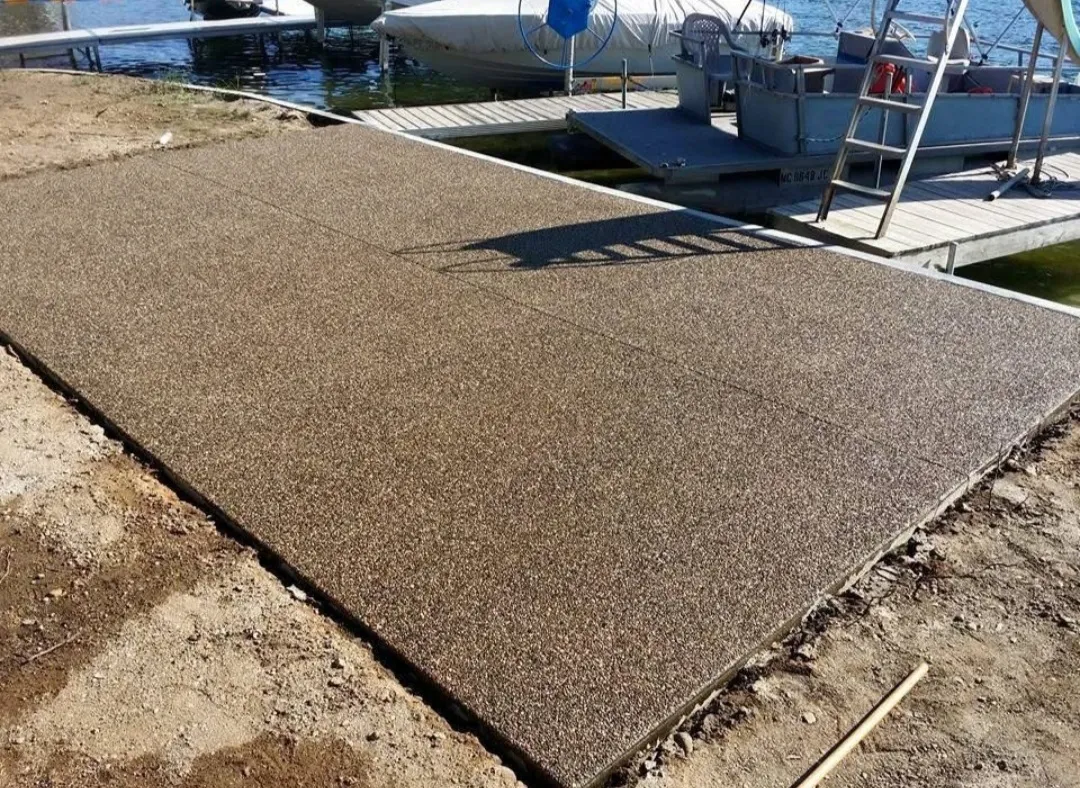 Newly installed, textured dock surface extending to the water, surrounded by dirt and wooden dock structures in the background.