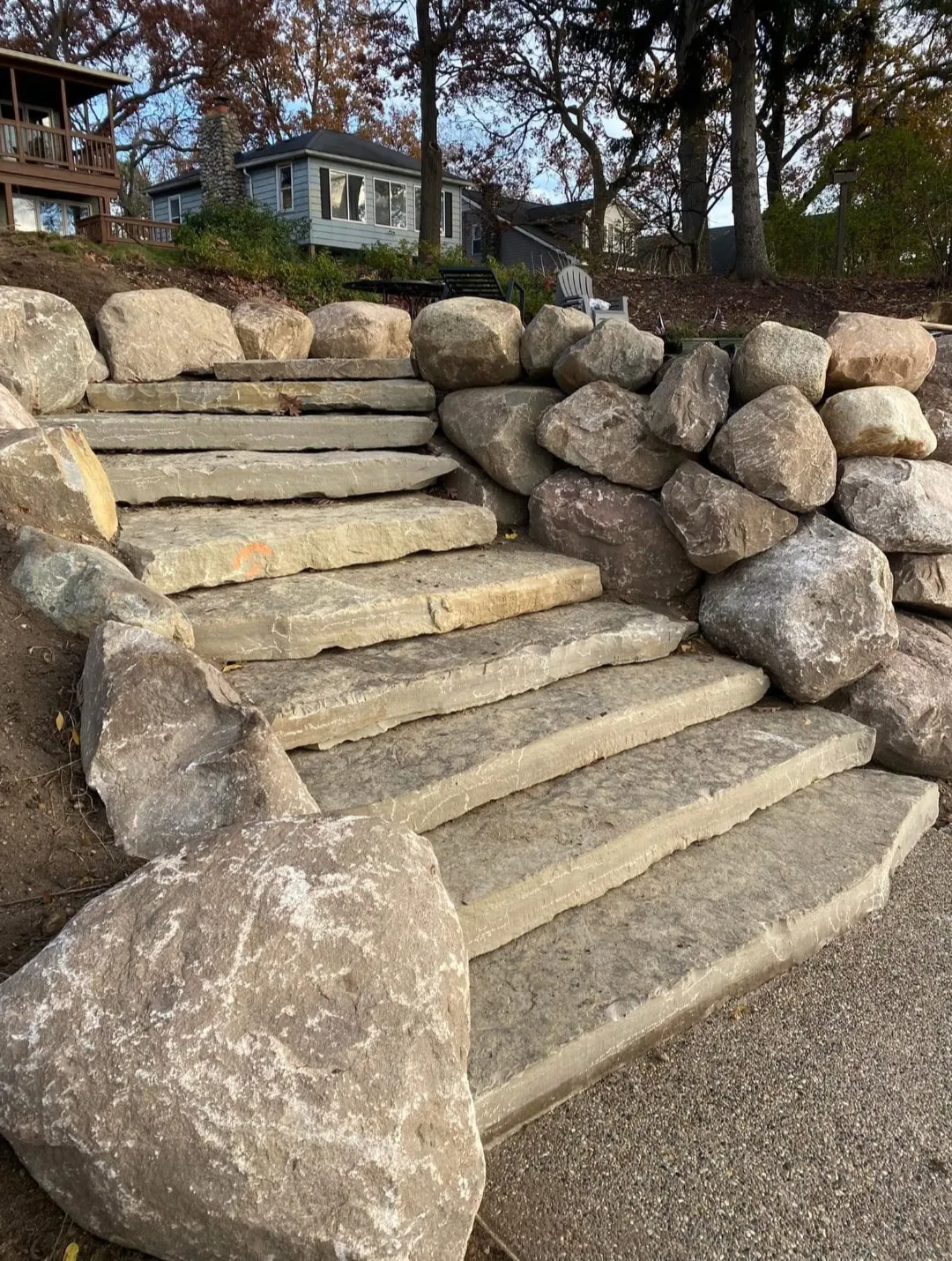 Stone steps leading up to a house, framed by large rocks and surrounded by trees, creating a rustic outdoor pathway.